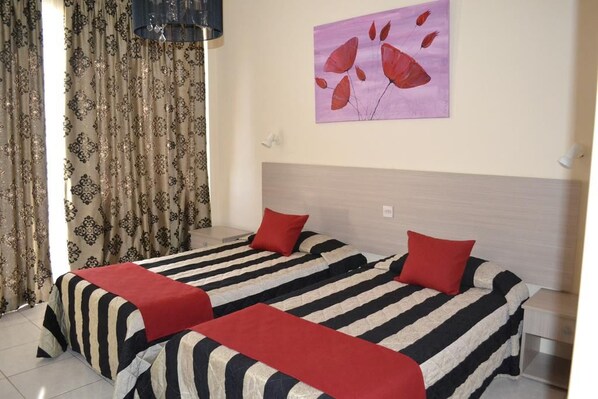 A hotel room with two beds, striped bedding, red pillows, a painting on the wall, and patterned curtains. - Tasiana Star (Limassol)