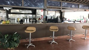 Uma área de bar com banquetas, balcão e cozinha ao fundo.