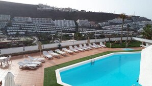 Área de piscina no terraço com espreguiçadeiras e vista para uma cidade costeira.