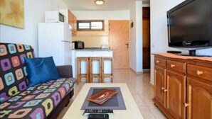 Sala de estar com sofá, mesa de centro, televisão e área de cozinha com armários e micro-ondas.