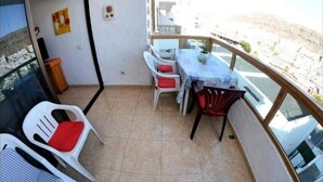 Uma varanda com mesa e cadeiras, uma pequena lata de lixo e vista para a paisagem.