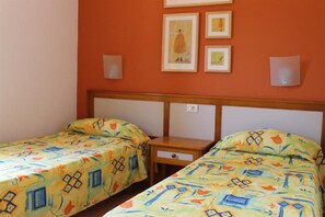 A room with two single beds, each with a patterned bedspread. There are framed pictures on the wall above the beds.