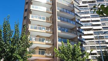 Un edificio de varios pisos con balcones, un café en la planta baja y un estacionamiento.