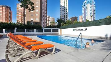 Una piscina con tumbonas, rodeada de edificios altos y una pared con el logotipo de una empresa.