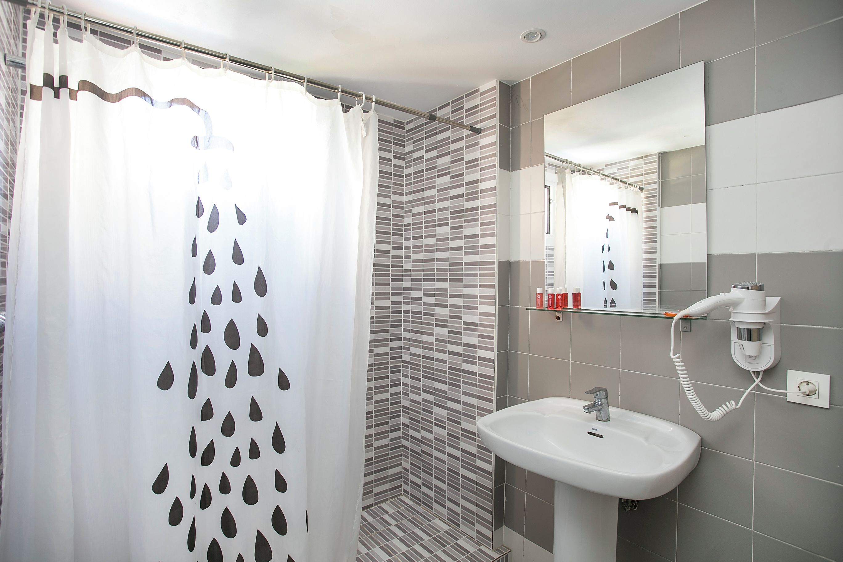 Un baño con cortina de ducha, paredes de azulejos, un lavabo y un espejo.