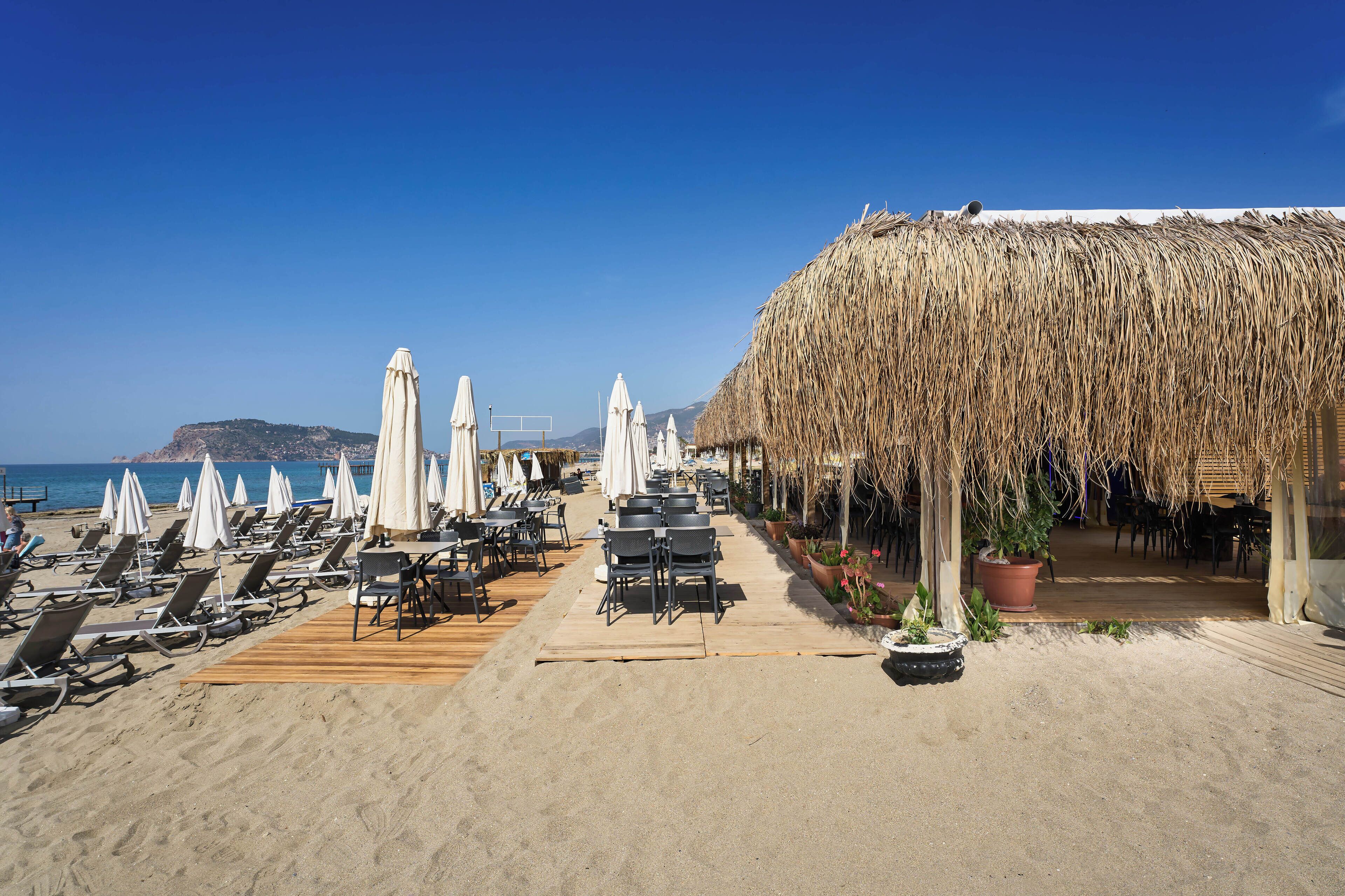 Un restaurante frente al mar con mesas al aire libre, sombrillas blancas y una estructura de techo de paja.