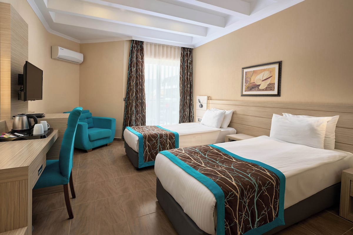 A hotel room with two beds, a desk, a chair, and a TV.