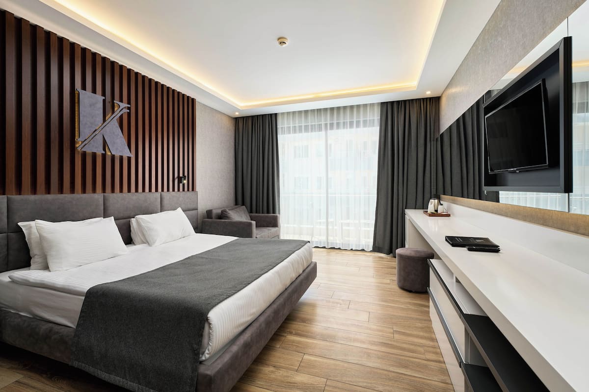 A modern hotel room with a large bed, a sofa, a TV, and a view of the city.