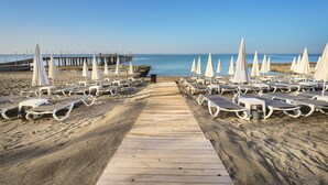 Una playa con filas de tumbonas y sombrillas, un muelle de madera que conduce al agua y un molo al fondo.
