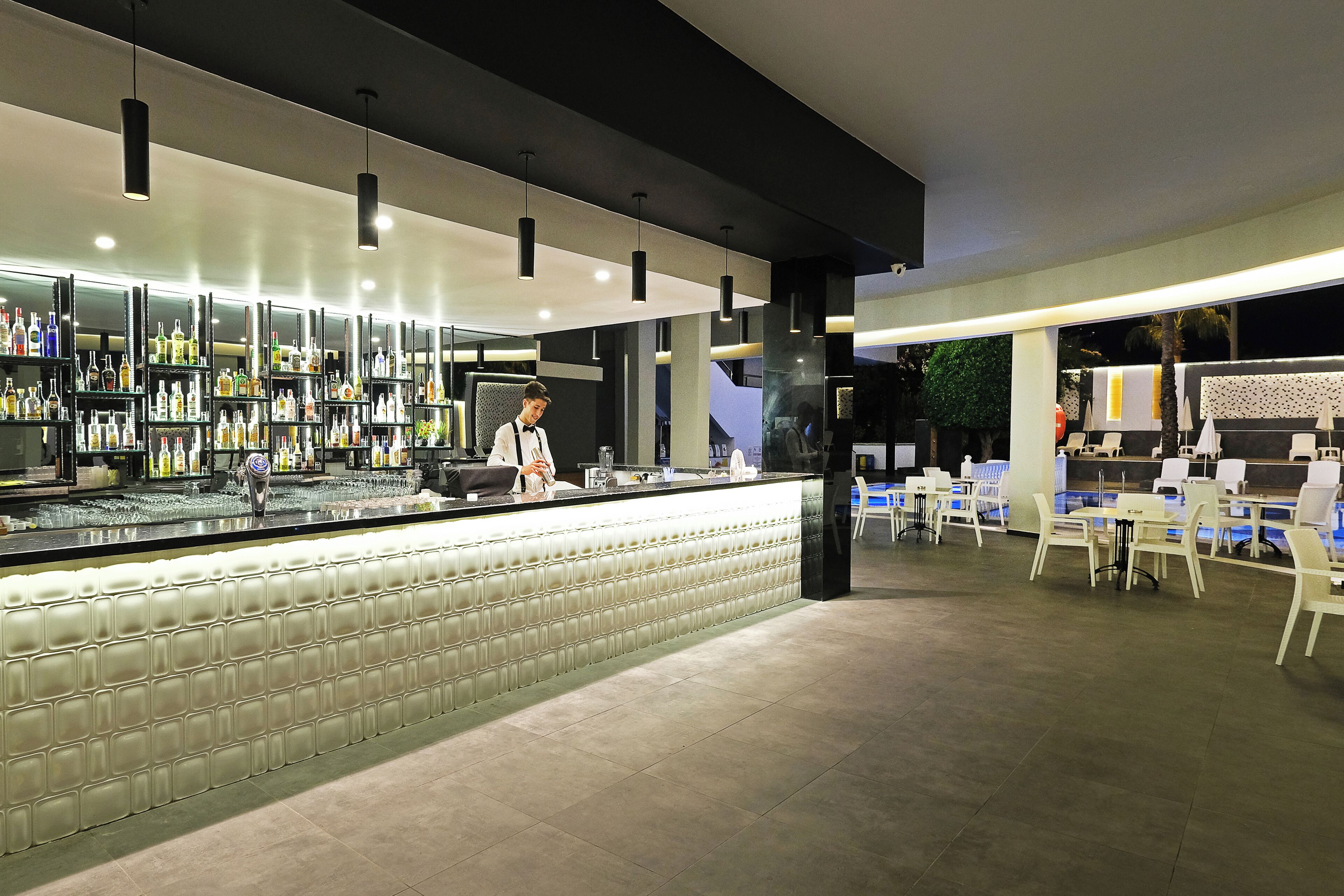 Zona de bar amb barra, prestatges plens de botelles i seients.