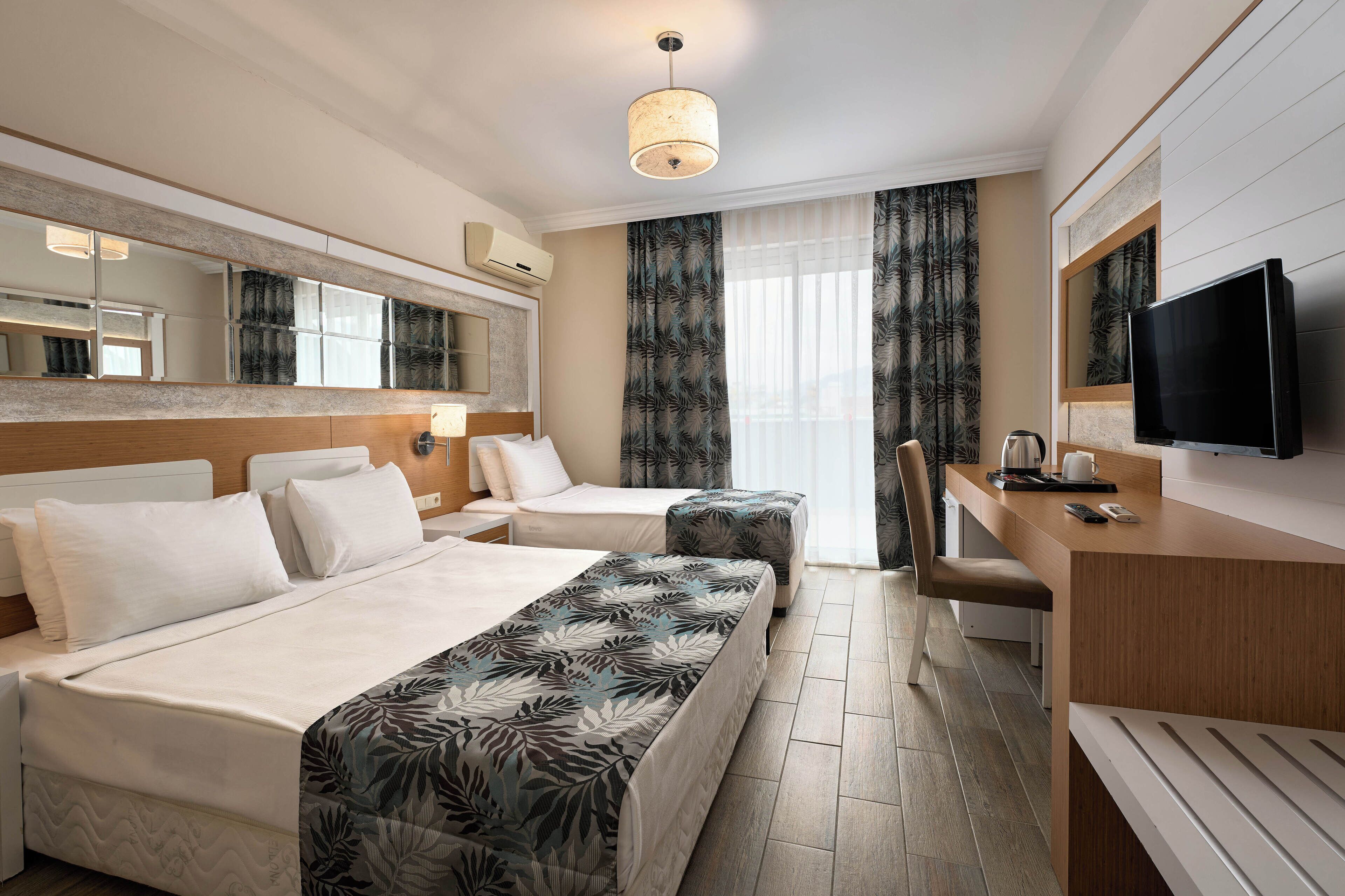 A hotel room with a bed, a desk, a chair, a TV, and a window with curtains.