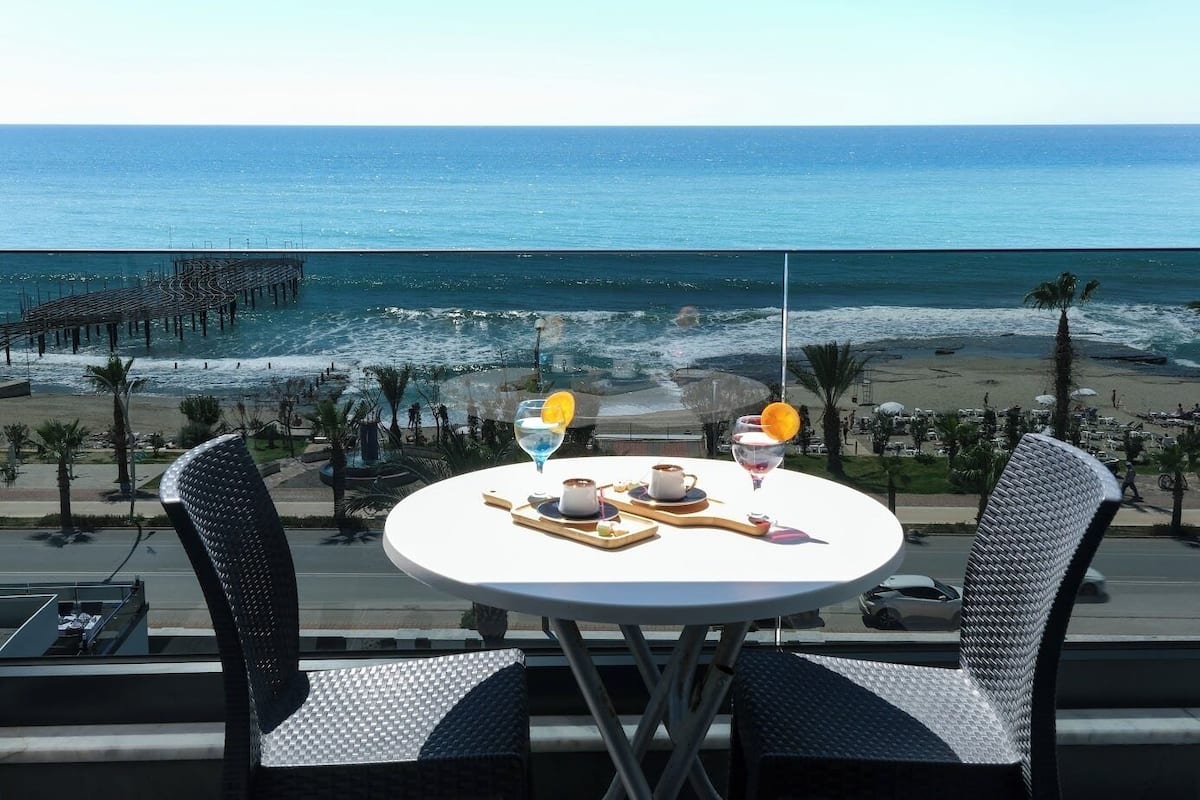 A table with two chairs, a tray with a cup and a glass, and a view of the beach and ocean.