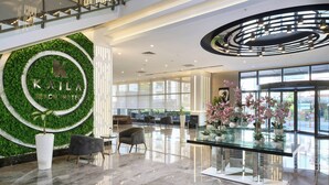 Un moderno vestíbulo de hotel con una pared verde, una recepción, zona de estar y una mesa de centro de vidrio con plantas.
