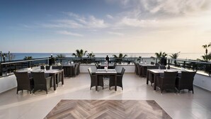 Una terraza en la azotea con mesas y sillas para comer, con vistas al océano.