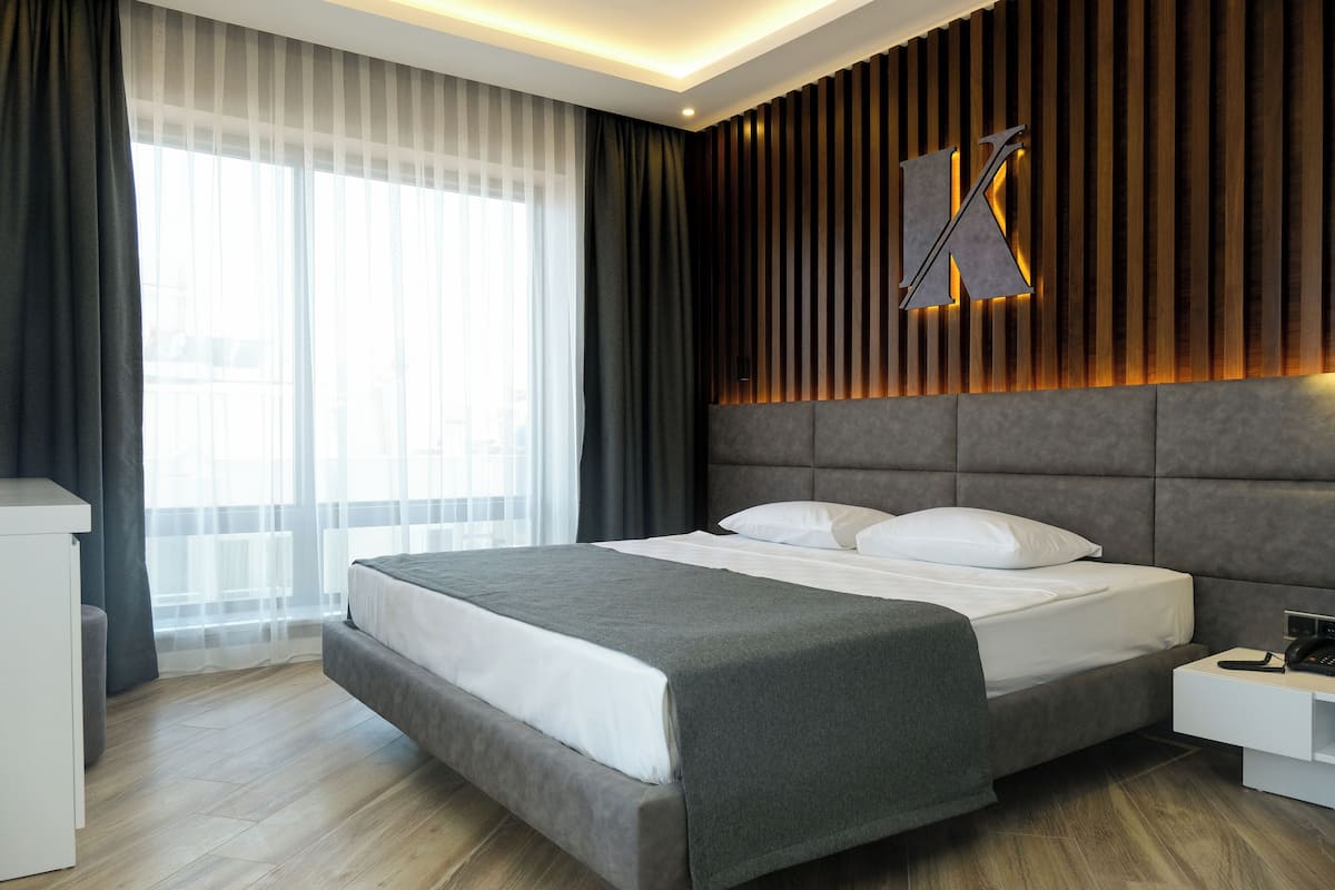 A modern hotel room with a large bed, a desk, and a large window with curtains.