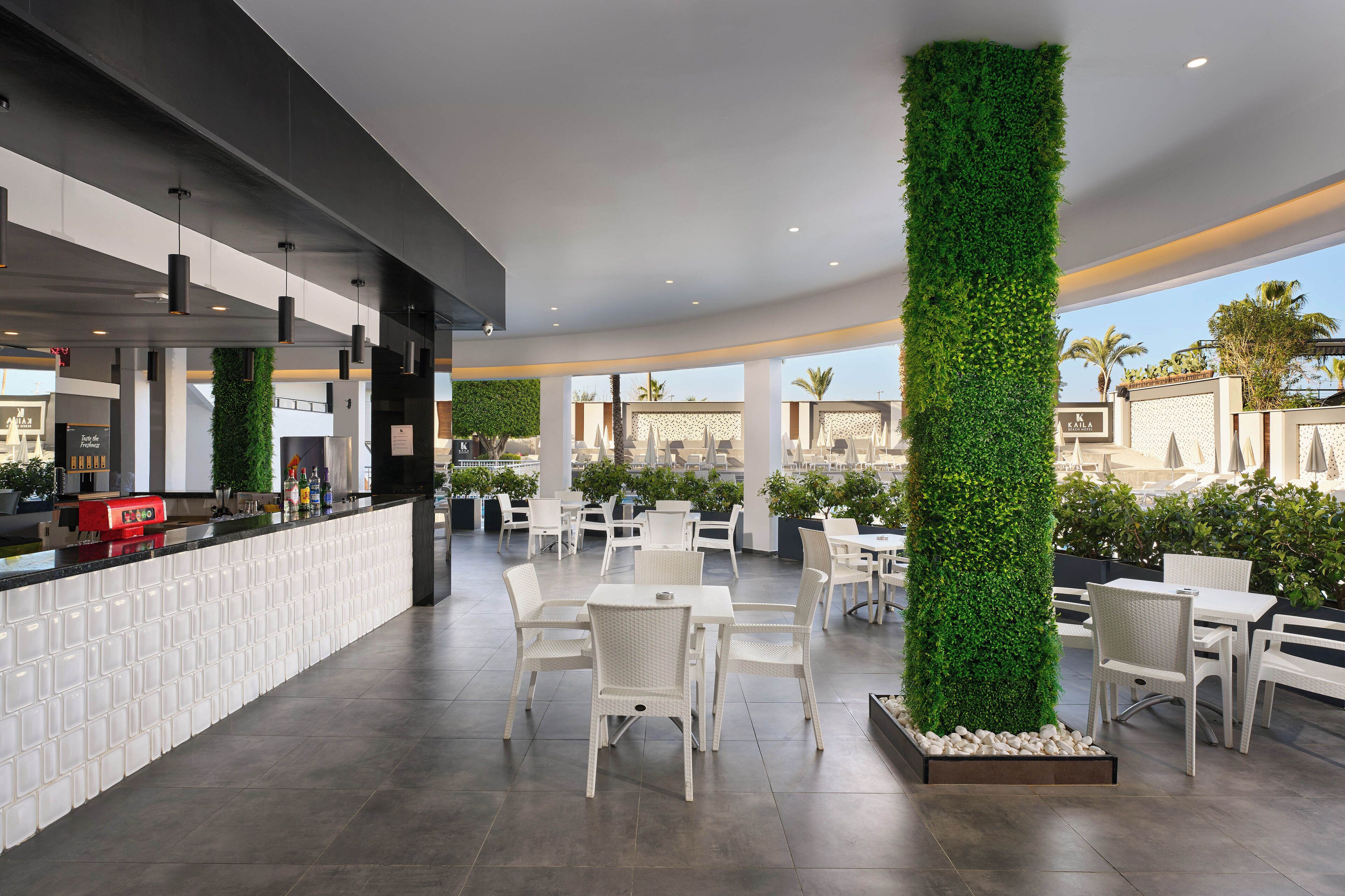 A modern indoor dining area with white furniture, a bar counter, and green vertical gardens.