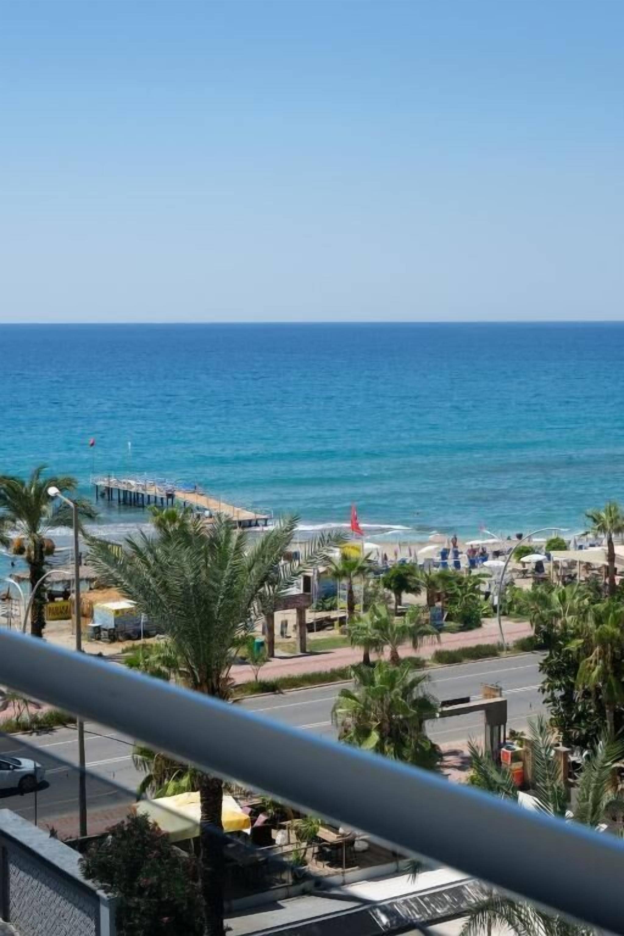 A coastal view with a pier extending into the sea, palm trees, and a clear sky.