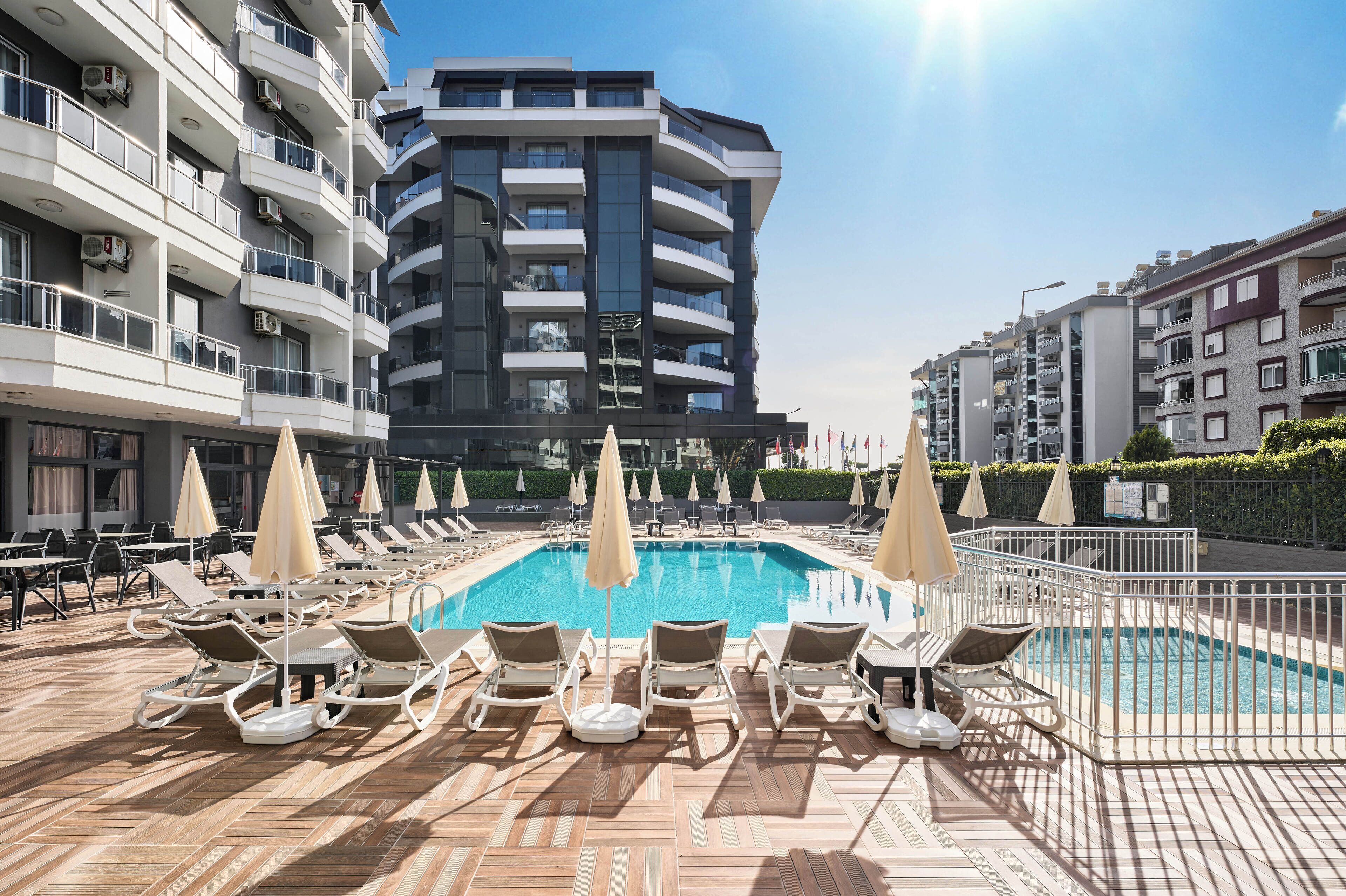 Un espace piscine aménagé sur le toit, avec des chaises longues et des parasols, entouré d’immeubles modernes.