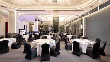A spacious banquet hall with multiple round tables, black chairs, and a modern chandelier.
