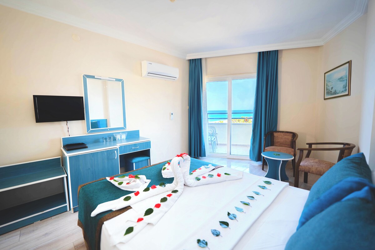 A hotel room with a bed, a desk, a chair, a TV, and a balcony with a view.