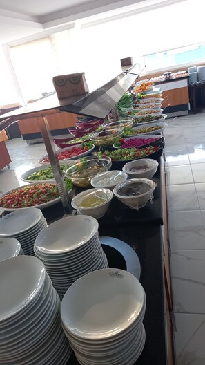 A buffet with various food options and stacked plates in the foreground. - Galaxy Beach Hotel (Alanya)
