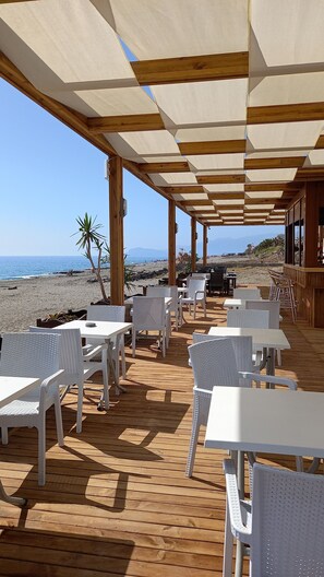 An outdoor seating area with tables and chairs, overlooking a beach and ocean.