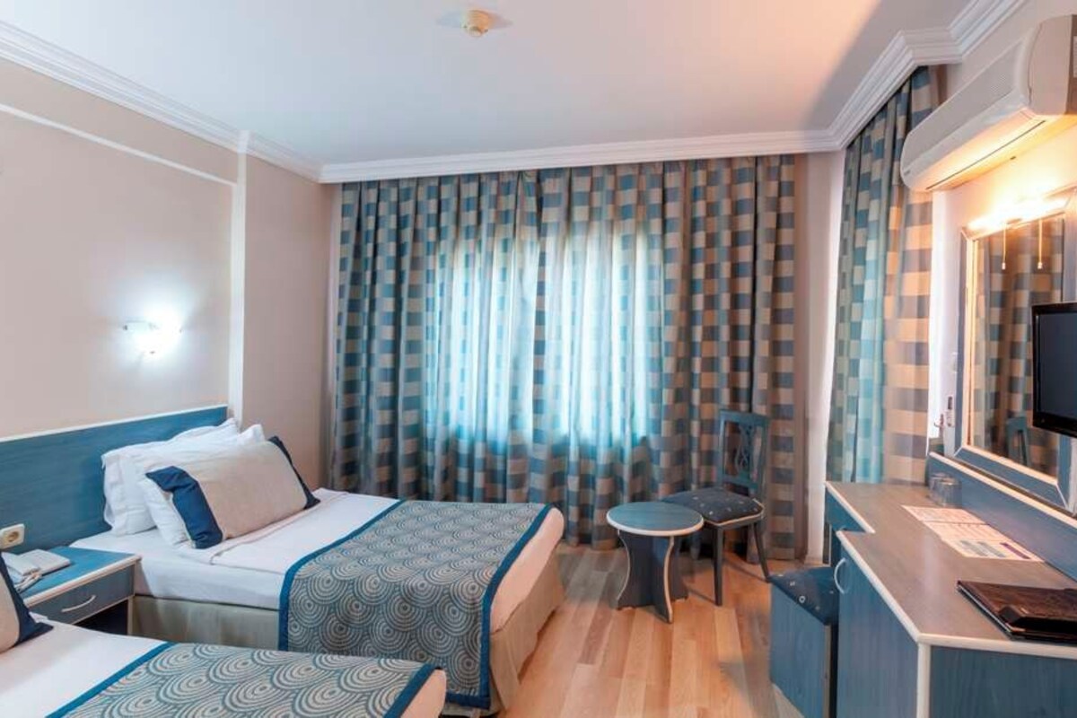 A hotel room with a bed, bedside table, TV, desk, and curtains.