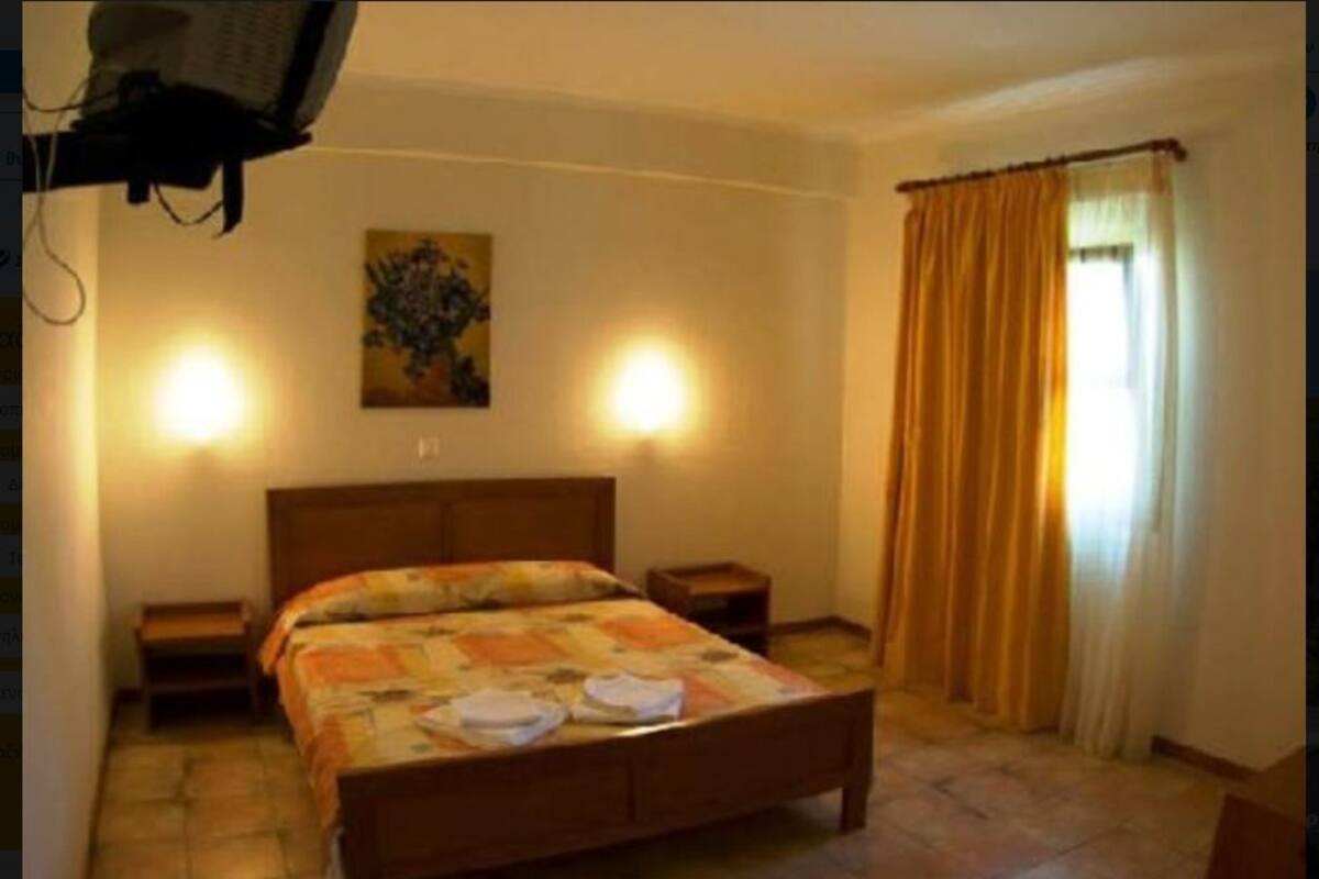 Ein Schlafzimmer mit einem hölzernen Bett, zwei Nachttischen, einem Schminktisch und einem Gemälde an der Wand, sowie einem Fenster mit Vorhängen.