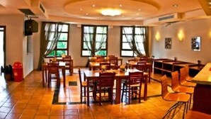 A spacious dining area with multiple tables and chairs, large windows with curtains, and a tiled floor. - Giga Mar (Kassandra)