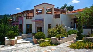 A two-story building with a covered patio area, surrounded by greenery and a stone-paved courtyard. - Giga Mar (Kassandra)