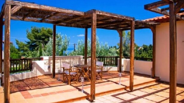 A covered outdoor patio with a wooden pergola, a table, and chairs. - Giga Mar (Kassandra)