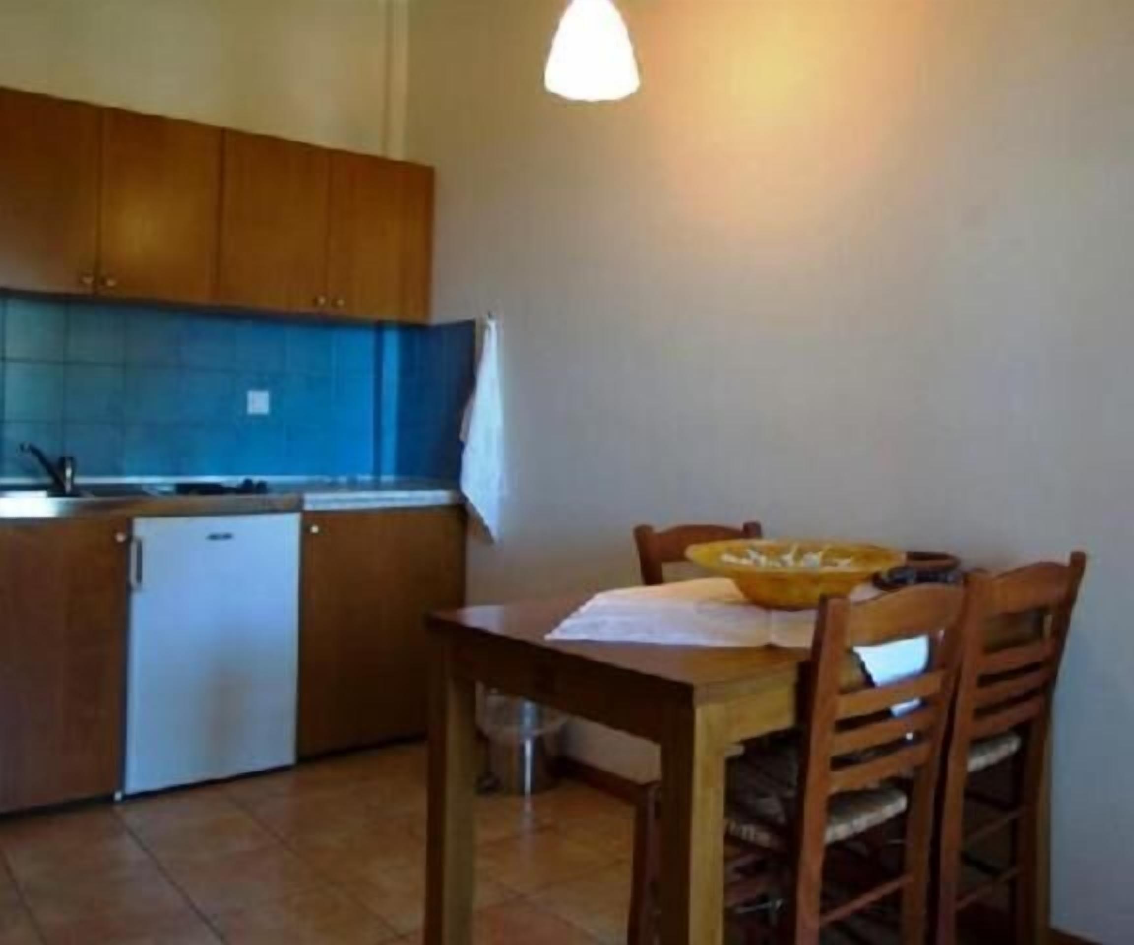 Una cucina compatta con mobili in legno, un piccolo frigorifero e un tavolo con sedie.