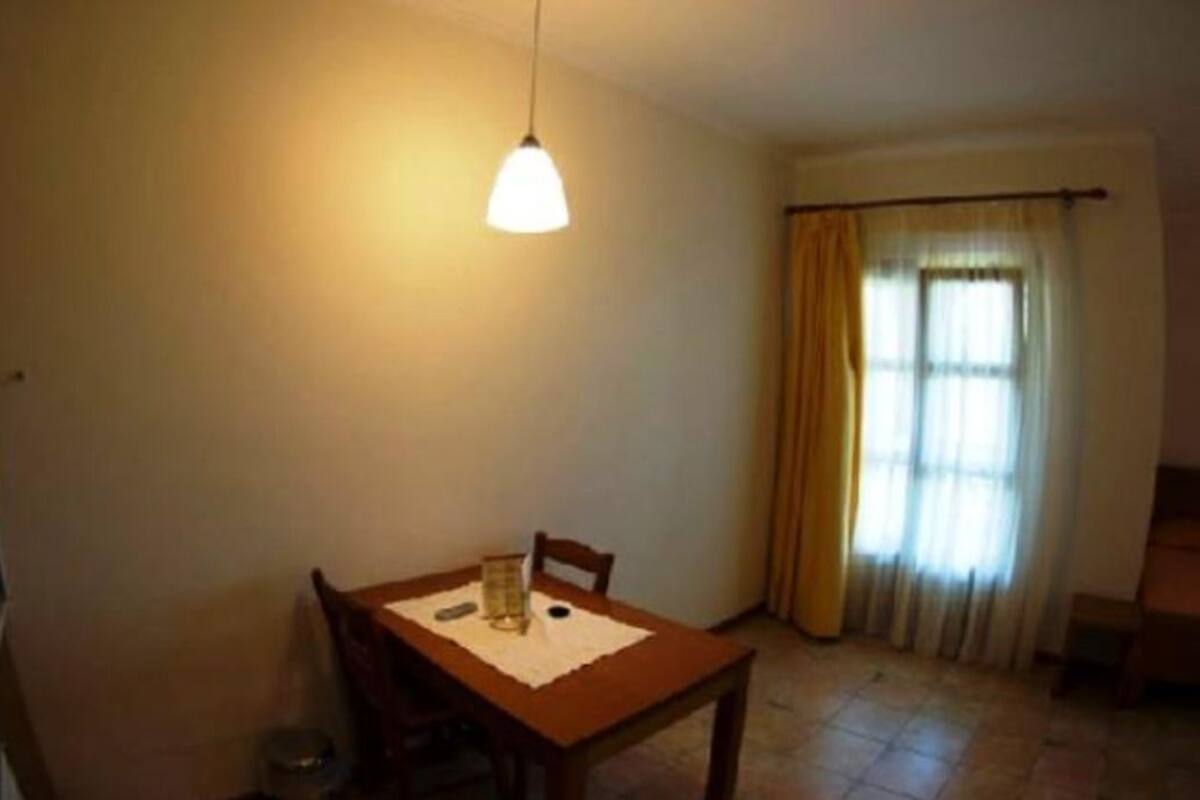 Ein Essbereich mit Tisch, Stühlen, einer Pendelleuchte, einem Fenster mit Vorhängen und einem Fliesenboden.