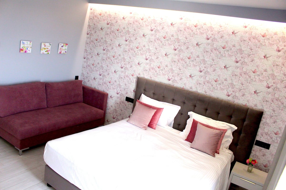 A bedroom with a bed, a red sofa, and a floral wallpaper.
