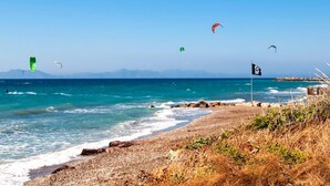 Une plage aux eaux d’un bleu limpide, un rivage rocheux et plusieurs cerfs-volants qui volent dans le ciel.