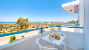 Un balcon avec une table préparée pour le petit-déjeuner, offrant une vue sur une route côtière et le paysage environnant.