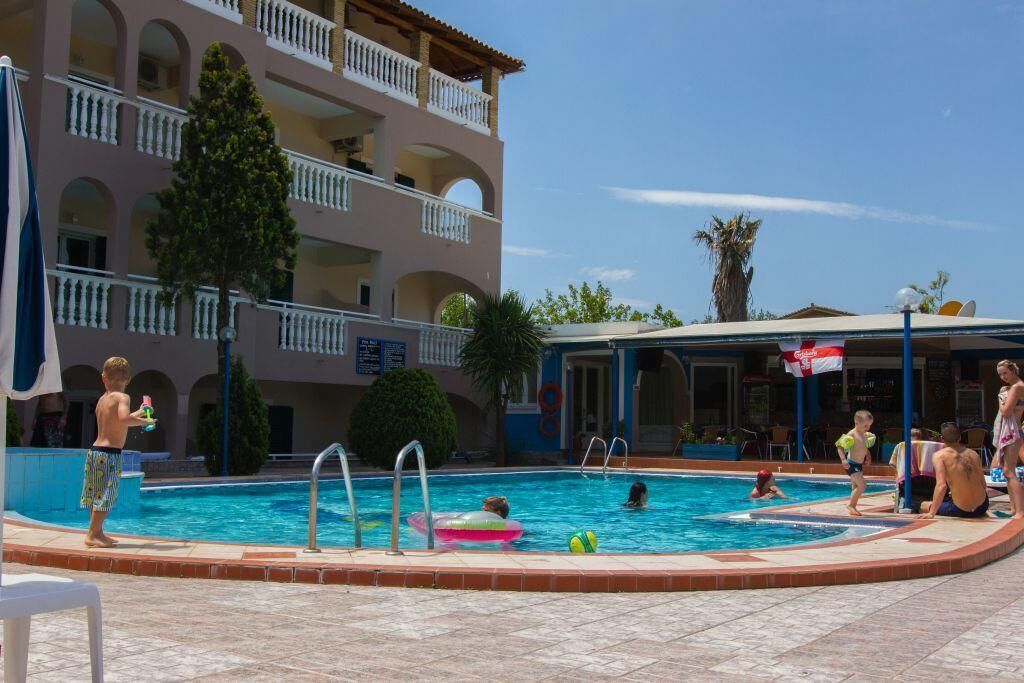 A swimming pool area with a building in the background, a lifeguard tower, and a palm tree.