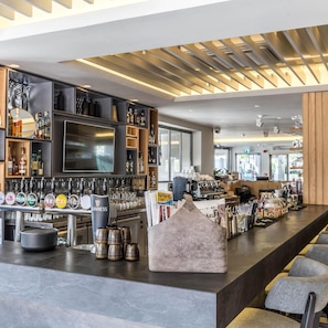 Zona de bar moderna con una barra alargada, múltiples grifos y una pantalla de televisión.