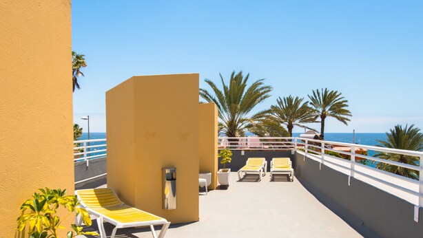 Un balcón con sillones amarillos, barandal blanco y vista al mar.
