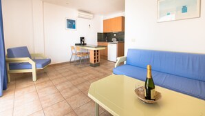 Un espacio habitable compacto con kitchenette, una zona de comedor con sillas, un sofá y una mesa con botella y vaso.