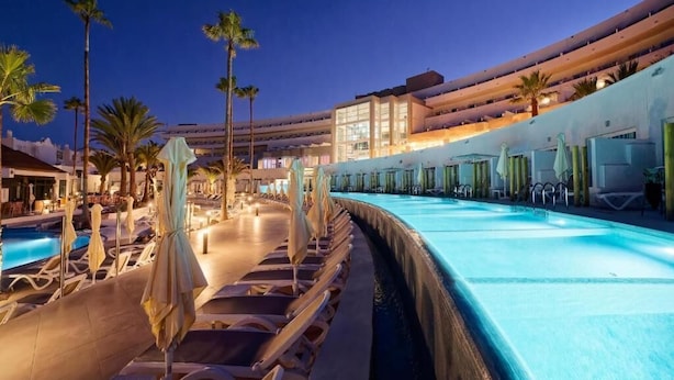 A hotel pool area with lounge chairs and umbrellas, surrounded by palm trees and a multi-story building with balconies. - LABRANDA Hotel Golden Beach  (Pajara)