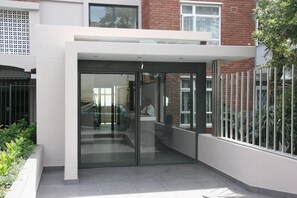 A modern building entrance with a glass door, a white exterior, and a brick wall in the background. - Cascades Suites (Cape Town)