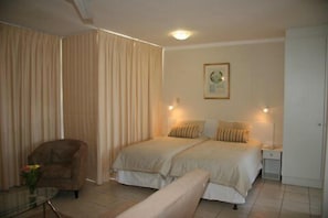 A bedroom with two beds, a chair, a bedside table, and a picture on the wall.
