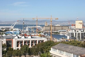 A coastal cityscape with modern buildings, a marina, and construction cranes.
