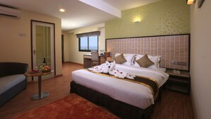 A hotel room with a large bed, a desk with a chair, a small table with a fruit bowl and wine glasses, and a sofa. - Uptown Hotel (Yangon)