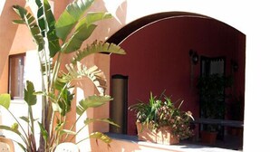An outdoor area with a red wall, a large plant, a bench, and a potted plant. - Le Terre di San Domenico (Augusta)