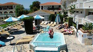 Piscina com espreguiçadeiras e guarda-sóis, rodeada por edifícios.
