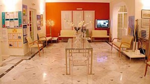 Um saguão de hotel com piso de mármore, uma mesa com tampo de vidro e dois sofás.