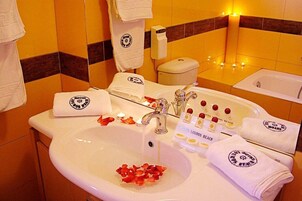 Un baño de hotel con lavamanos, inodoro y bañera. Hay toallas y artículos de aseo en el mostrador.