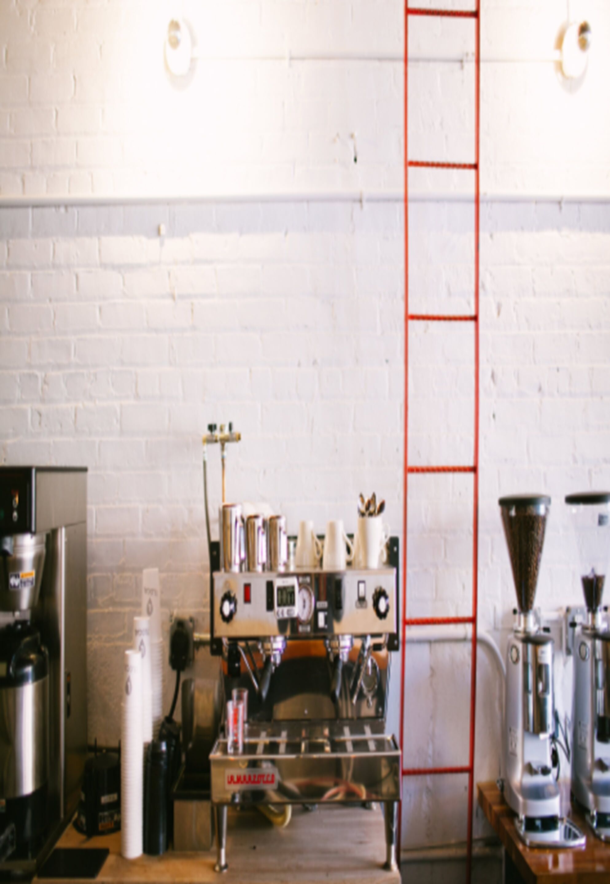 A coffee shop interior with espresso machines, a ladder, and a brick wall.